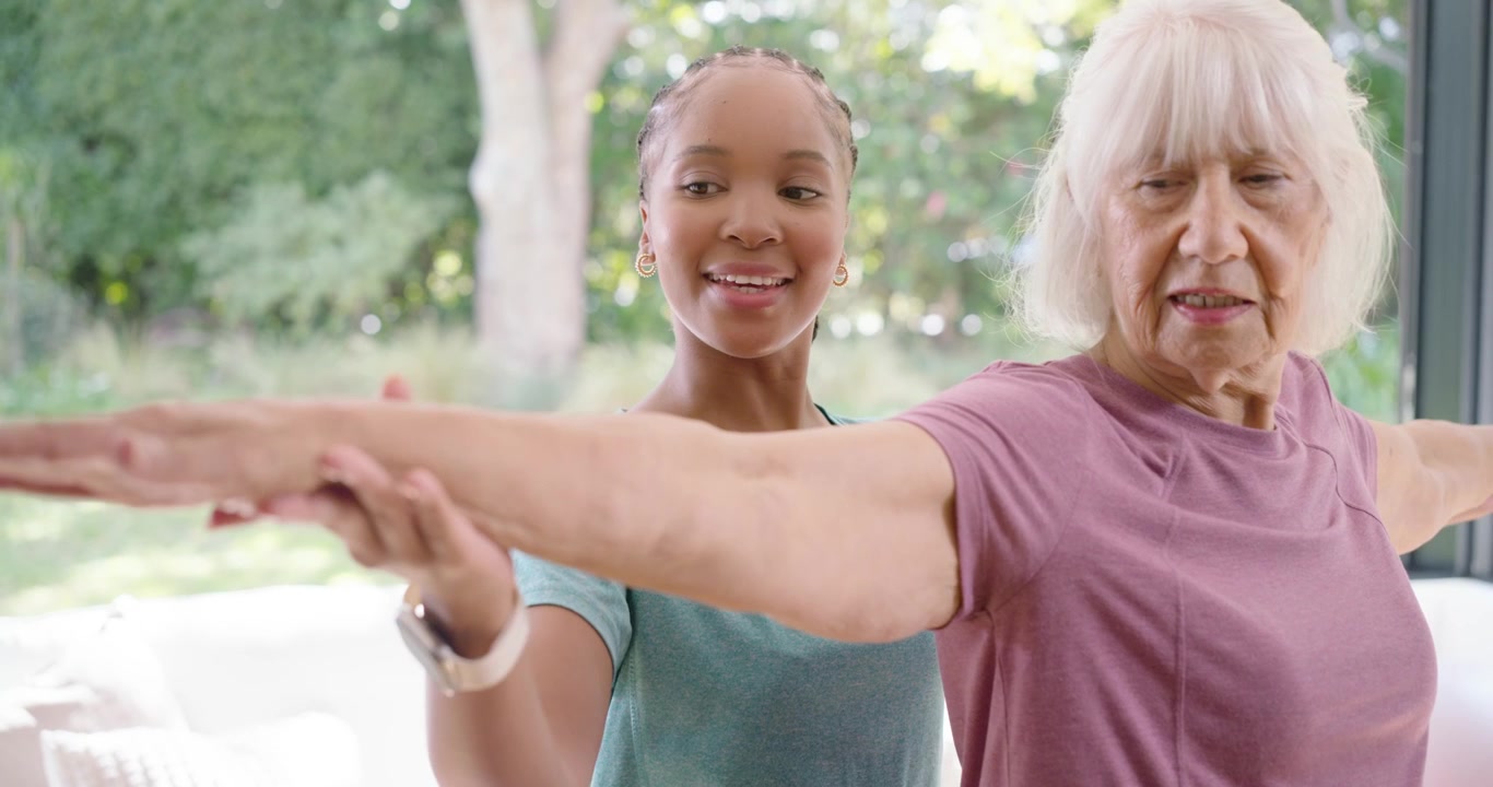 African American caregiver and senior woman holding arms, guiding T-pose near windows for balance