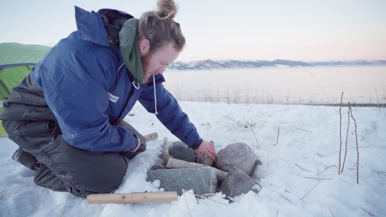 camper haciendo fuego fuera de la tienda rodeada de rocas en invierno