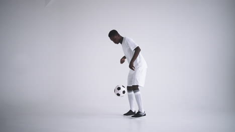 slow motion: one african man soccer player white jersey juggling in silhouette on white background. one black brazilian soccer football player man silhouette