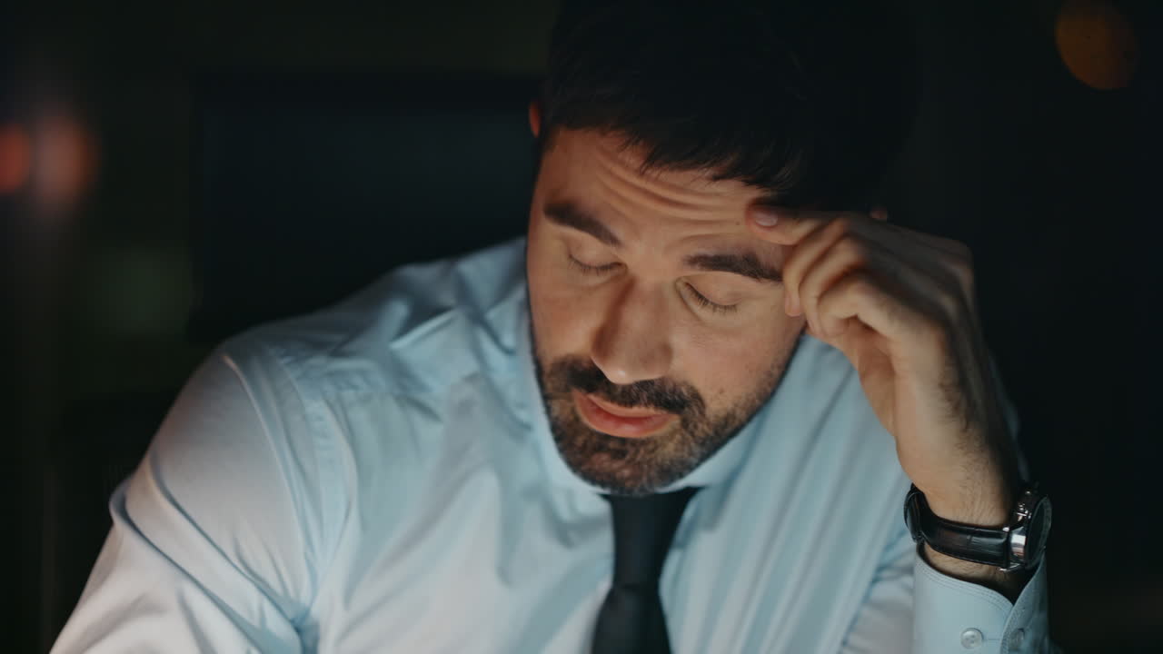 Primo piano di manager d'ufficio esausto seduto al lavoro di notte, preoccupato per i problemi.