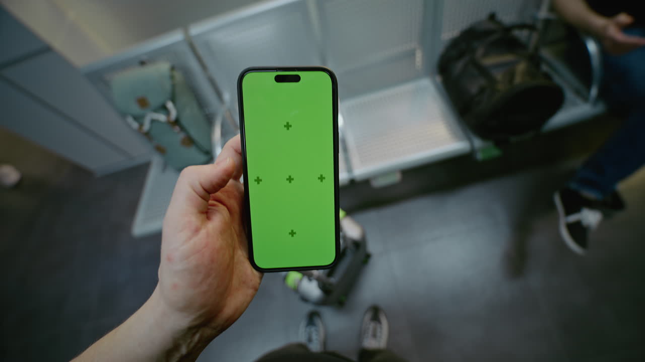 Person holding a phone with a green screen in an airport waiting area.