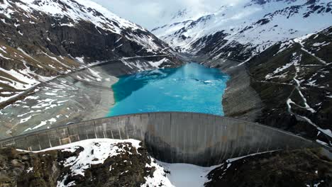 4k drone aerial tilt shot of vibrant blue glacial water of lac de moiry dam surrounded by massive snow covered mountains reflecting on lake in grimentz switzerland