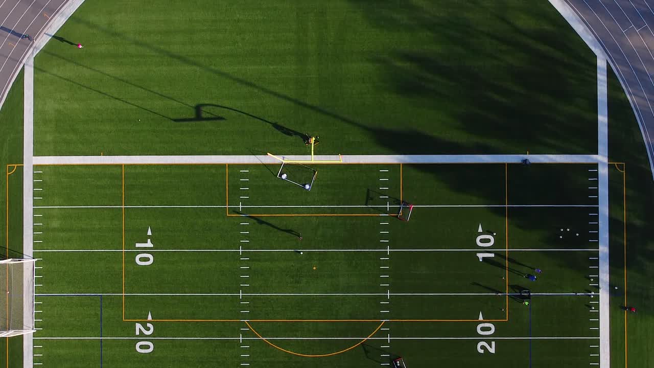 Coaches training kids to play soccer on multi-purpose football field with people walking and cycling on track