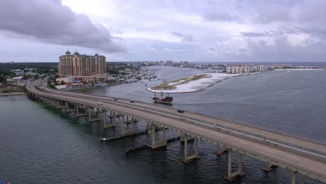 Fliegender-Blick-über-Die-Destin-Fl-Brücke-In-Richtung-Hafen-Und-Ein-Piratenschiff,-Das-In-Das-Harbourwalk-Village-Einfährt