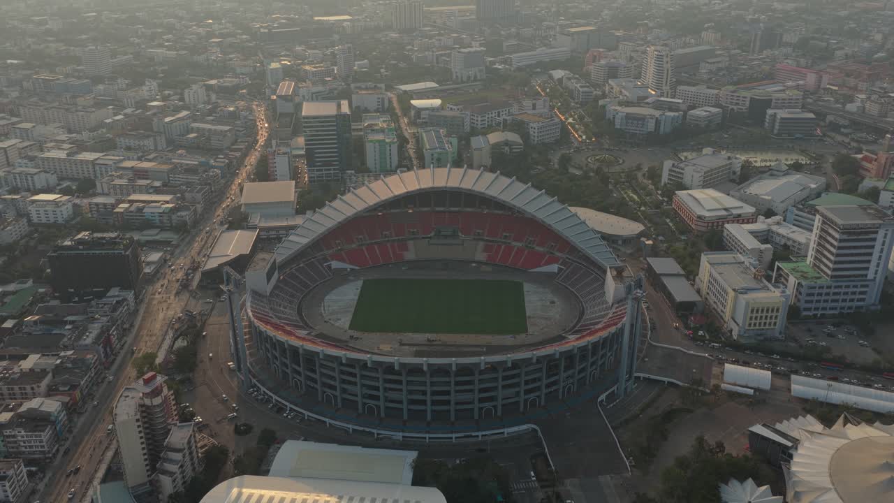 Ripresa aerea che vola all'indietro e si inclina verso l'alto, rivelando lo Stadio Nazionale Rajamangala e lo skyline nebbioso circostante della città di Bangkok.