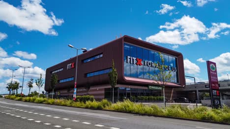 motion time-lapse from road traffic to modern fitness studio building with clouds moving across sunny blue sky
