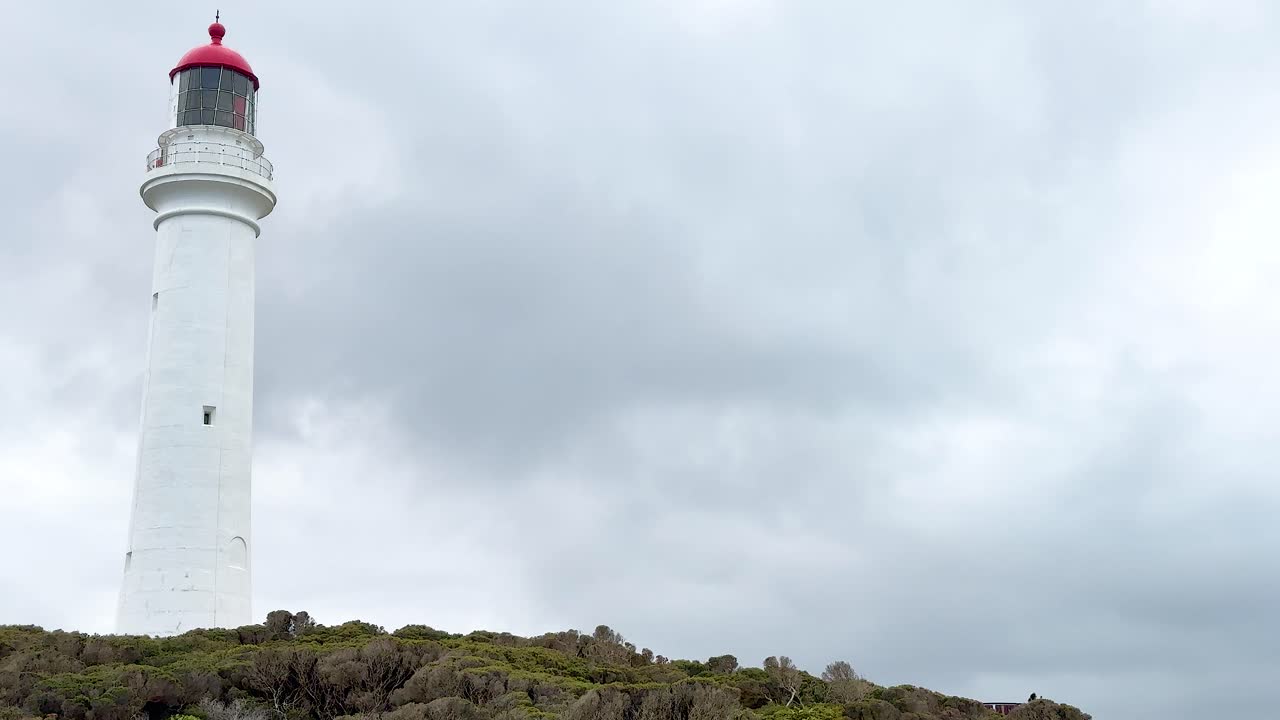 A tall white lighthouse stands against a cloudy sky on the Great Ocean Road, Victoria, Australia