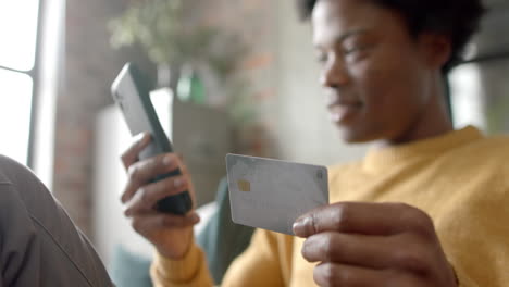 happy african american man sitting on sofa using smartphone for online shopping at home, slow motion