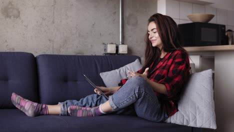 young beautiful brunette girl talking to someone through video call while sitting on a sofa