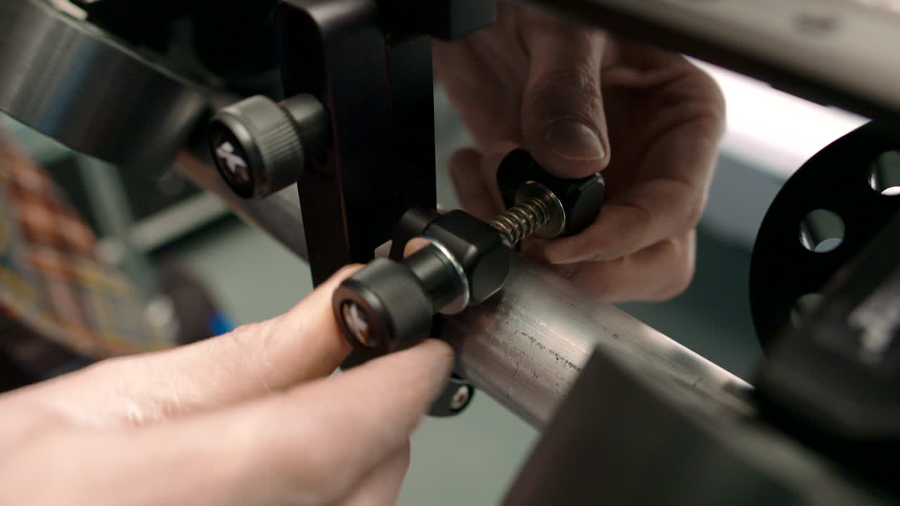 mano masculina apretando una abrazadera alrededor de un trozo de riel de velocidad de poste de andamio que forma parte de un sistema de carro deslizante de cámara