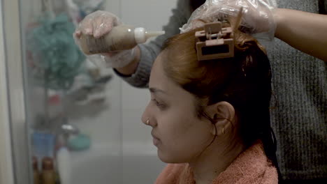 a close up side view of a young asian lady having her hair treated and coloured, the hairstylist carefully massaging the chemicals into her scalp in a bathroom