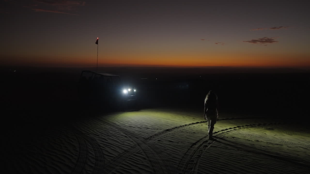 una chica camina hacia el boogie al atardecer en el desierto de huacachina, perú.