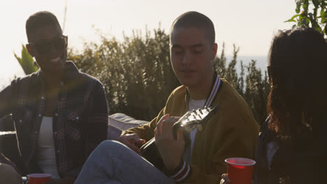 Un-Joven-Tocando-La-Guitarra-En-Una-Azotea-Con-Sus-Amigos.