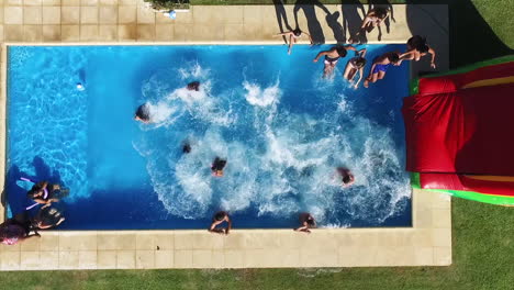 top down aerial view of people crowd jumping together in swimming pool on sunny summer day, high angle drone shot