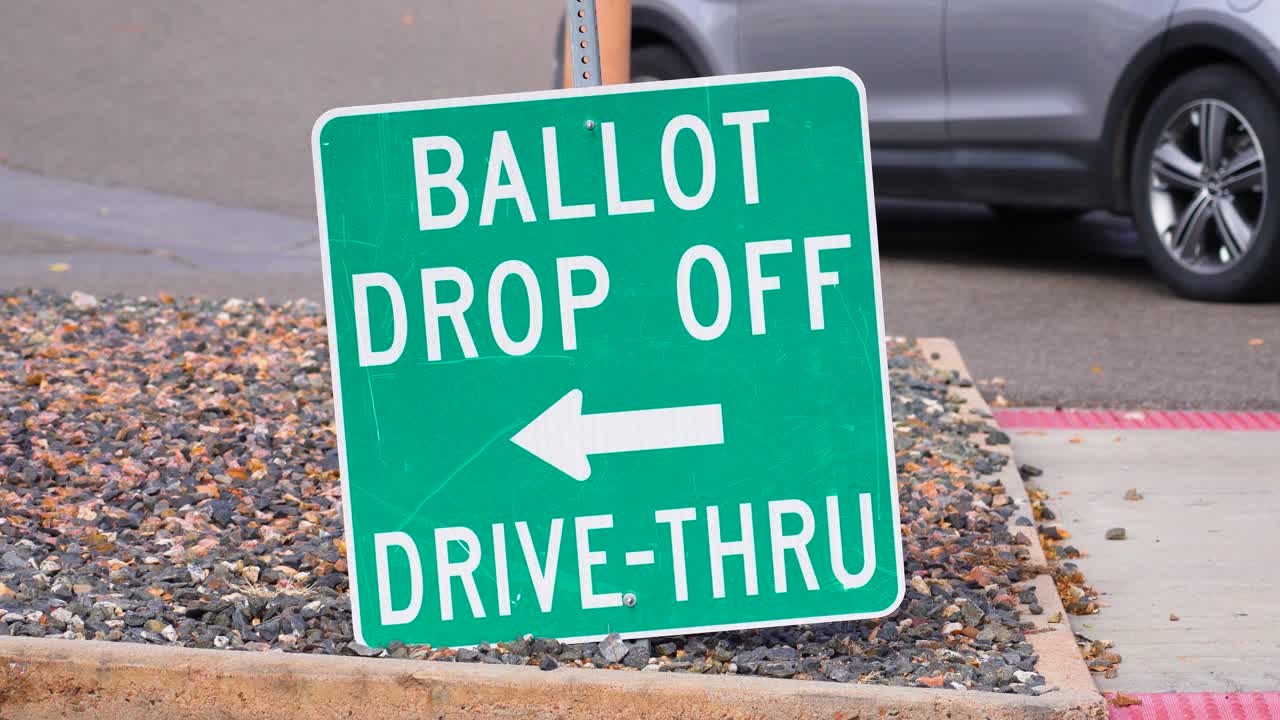 A ballot drop-off arrow sign guides voters to a secure drop box while cars pass, symbolizing civic duty, democracy, trust, accessibility, inclusivity, integrity, and responsibility