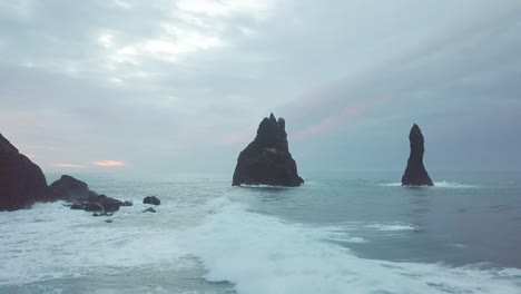 reynisdrangar rocks at reynisfjara beach next to vik i myrdal at south iceland. aerial drone shot flying over a cliff during sunrise. large storm waves crash rock. high resolution footage. 4k