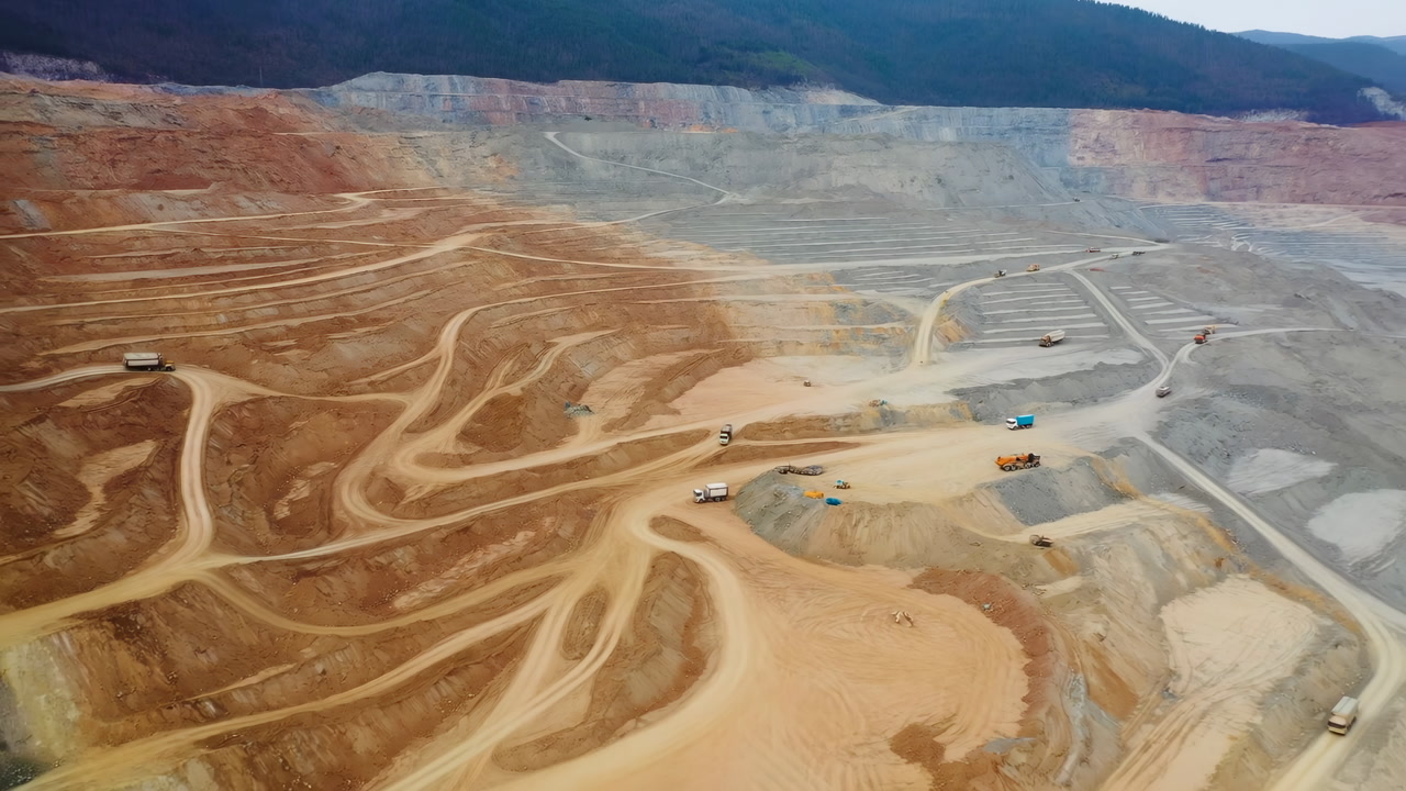 Aerial View Open Pit Mine Showing Terraced Benches, Winding Haul Roads, Heavy Trucks And Excavators Extracting