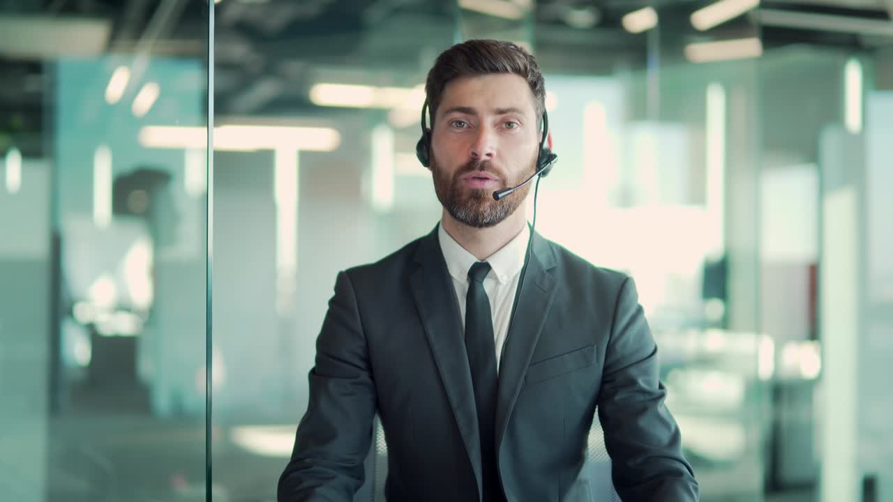 Kaukasisk forretningsmand som taler i jakkesæt med headset, kigger ind i kameraet. Online møde, konference, fjernundervisning