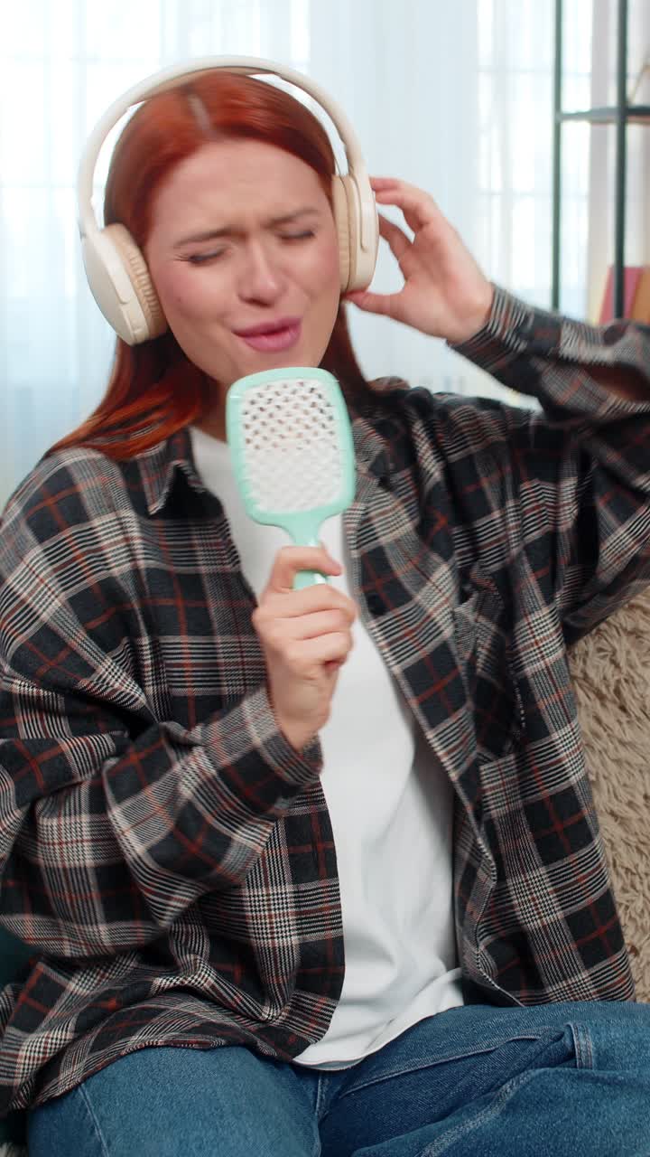 Donna seduta sul divano con le cuffie che canta con il pettine come microfono che si diverte con la gioia della musica