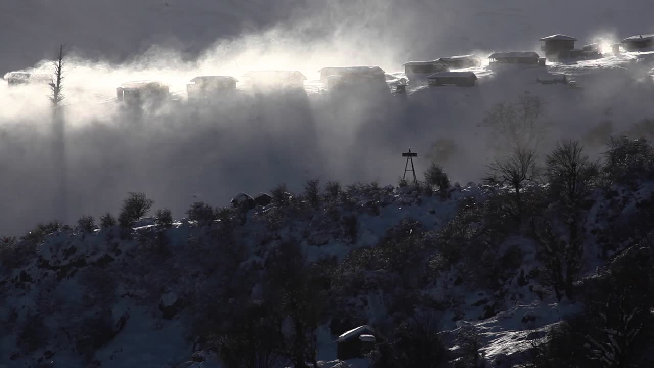 Bare trees wind move the freezing cold clouds fog in the town and villages with wooden cottage buildings in the highland landscape sun shine over the snow capped mountain and hill silhouette nature