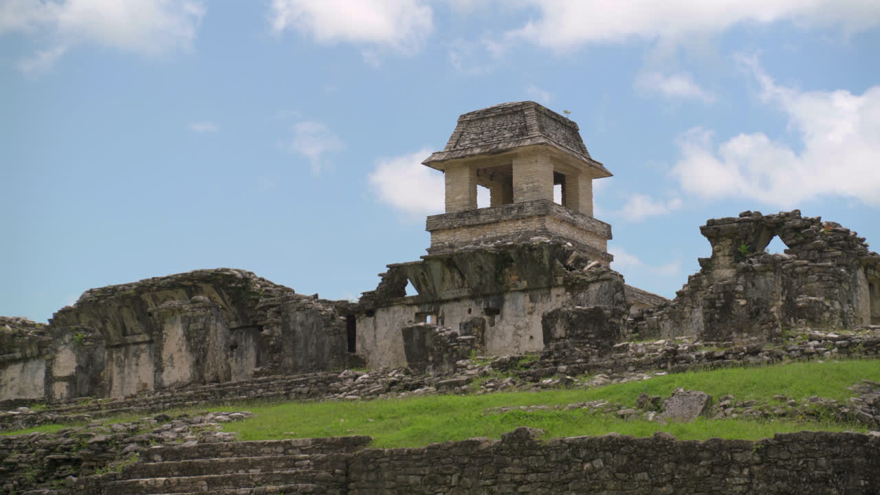 Palenque ruins showing stepped stone temples against open blue cloudy sky