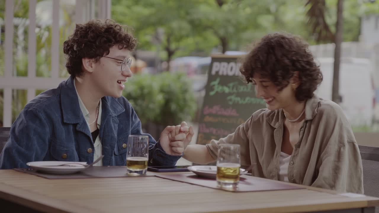 Two people holding hands and smiling at an outdoor cafe