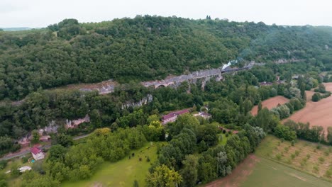 in the forest, a small steam train at the edge of the cliff moves slowly forward, smoke billowing from its chimney, carrying tourists to the station at martel in the lot region of france