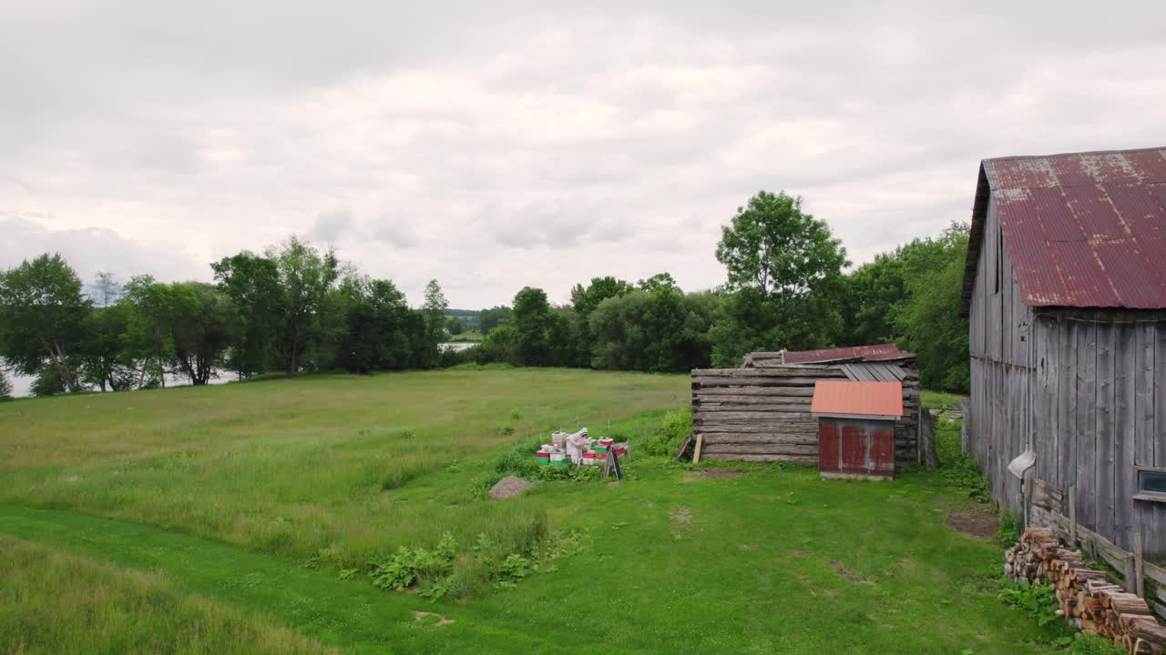 Aerial view of a beekeper working and collecting honey from a beehive, near an old barn