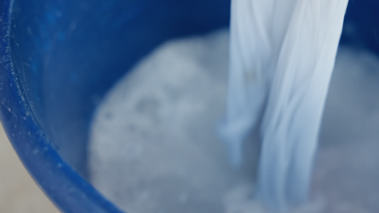染料不使用の布地が洗浄液に浸されている。石鹸と屋外の光を利用した優しい洗濯方法。穏やかな攪拌とすすぎを行う、日中の屋外での家庭の洗濯ルーティン。