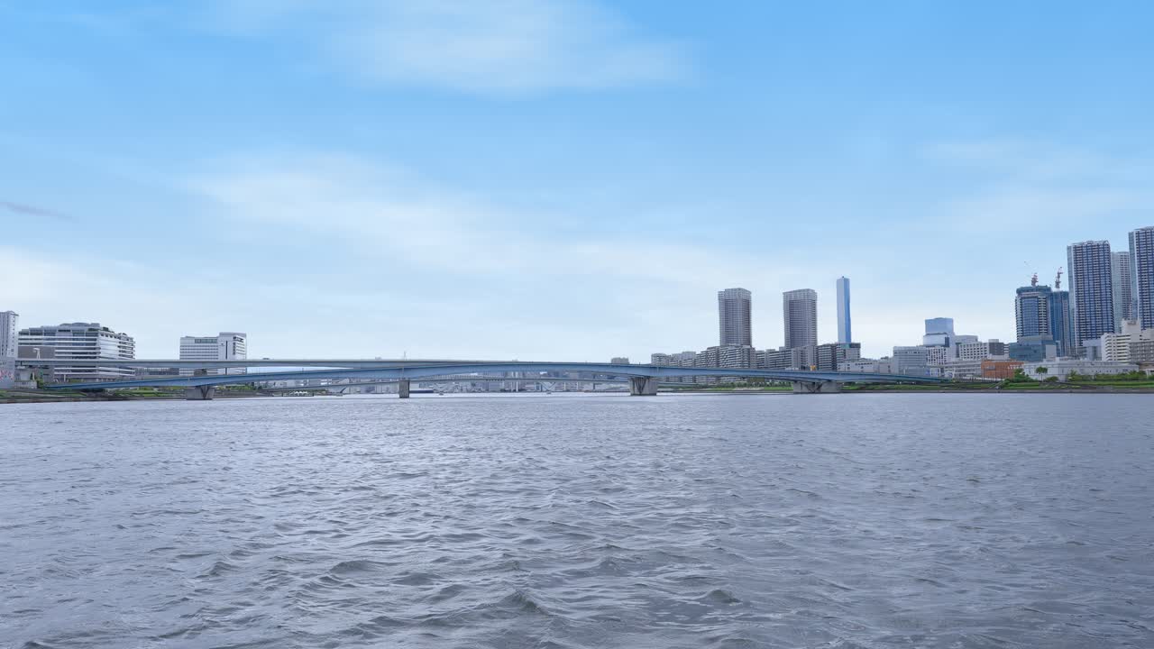 A wide, peaceful shot of Tokyo Bay with a modern bridge and the distant city skyline under a clear blue sky