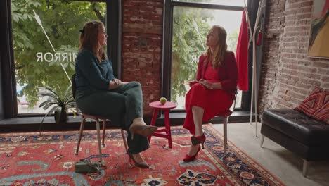 wide view of two woman sitting in a large room and talking to each other