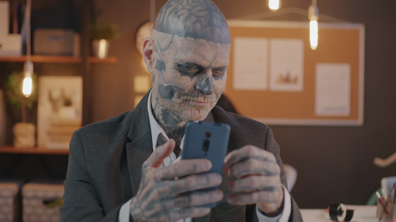 Tattooed Man Using Smartphone and Credit Card in Office