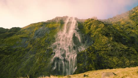 Serene-waterfall-with-clean-spring-water-flowing-down-a-cliff-with-rocks-covered-in-moss