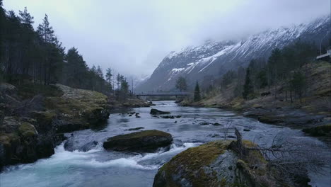 flying low over stream in norwegian wilderness surrounded by mountains and trees, aerial shot