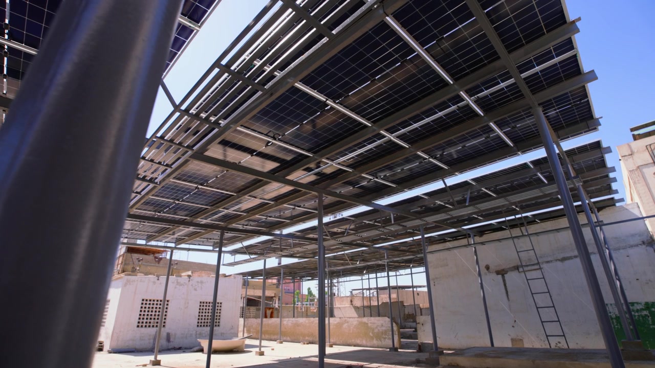 Ripresa dal basso con telecamera che segue un'installazione di pannelli solari sul tetto, mostrando telai di montaggio industriali sotto un'intensa luce solare.
