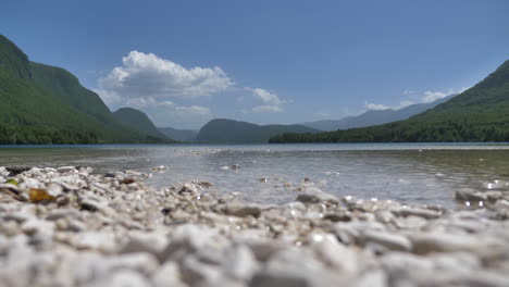 Statische-Nahaufnahme-Von-Klarem-Wasser,-Kleinen-Felsen-Und-Wunderschönen-Grünen-Hügeln-Und-Blauem-Himmel-Dahinter