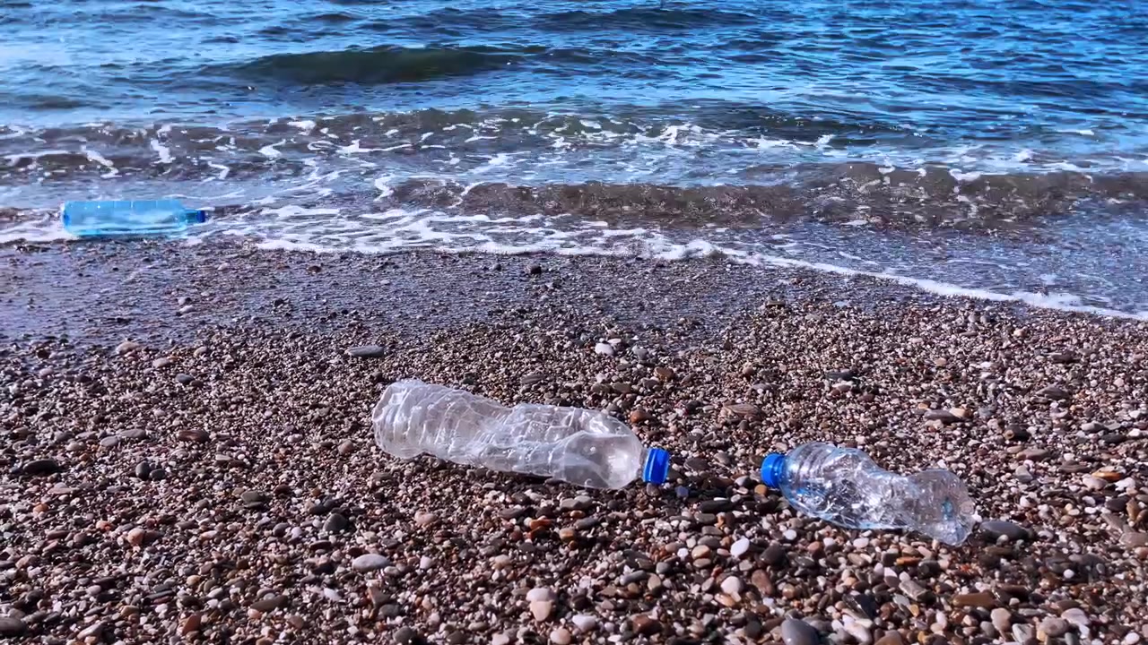 Bottiglie di plastica abbandonate che giacciono su una spiaggia di ciottoli vicino alle onde dell'oceano.