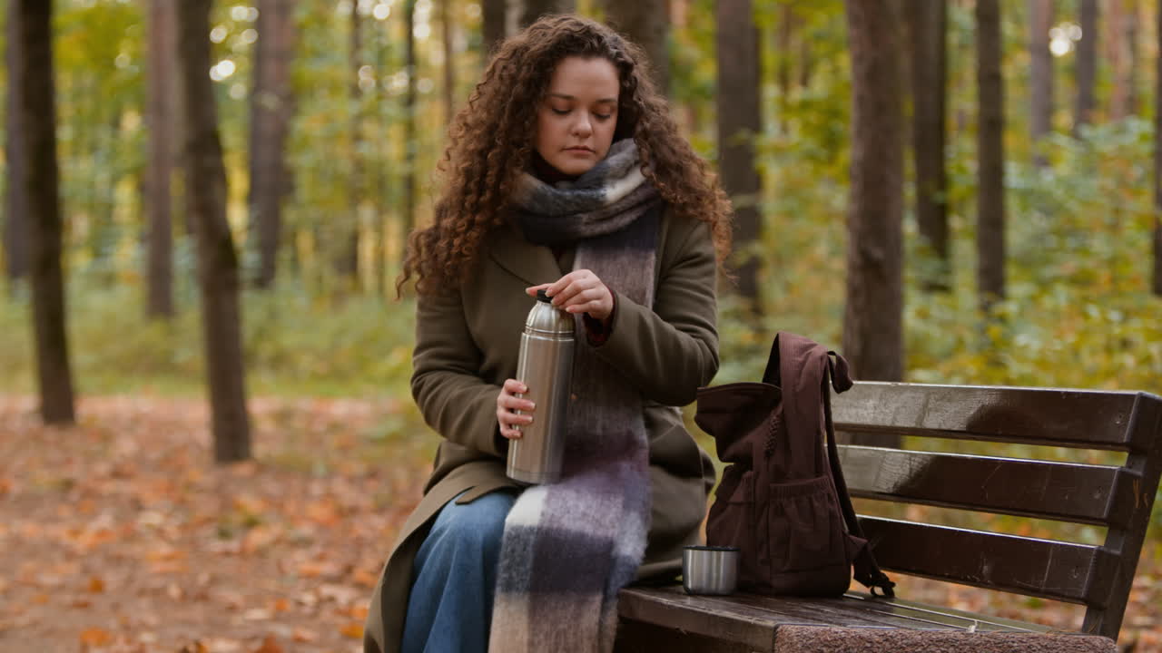 Woman with Thermos and Backpack Resting on Bench in Autumn Park
