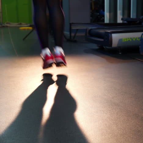 back view of woman's legs in athletic leggings and comfortable sport outfit jumping rope on a sport club. fitness female doing skipping workout