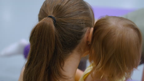 intimate moment between a mother and daughter embracing each other warmly, with the subtle background activity of someone exercising in a gym setting