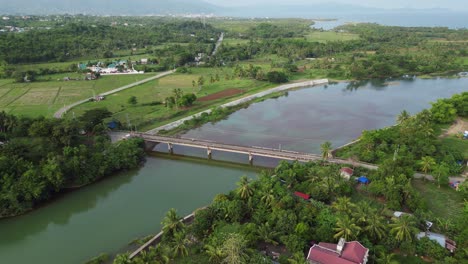 aerial pullback of scenic rural village community and bridge over a large river in bicol, philippines