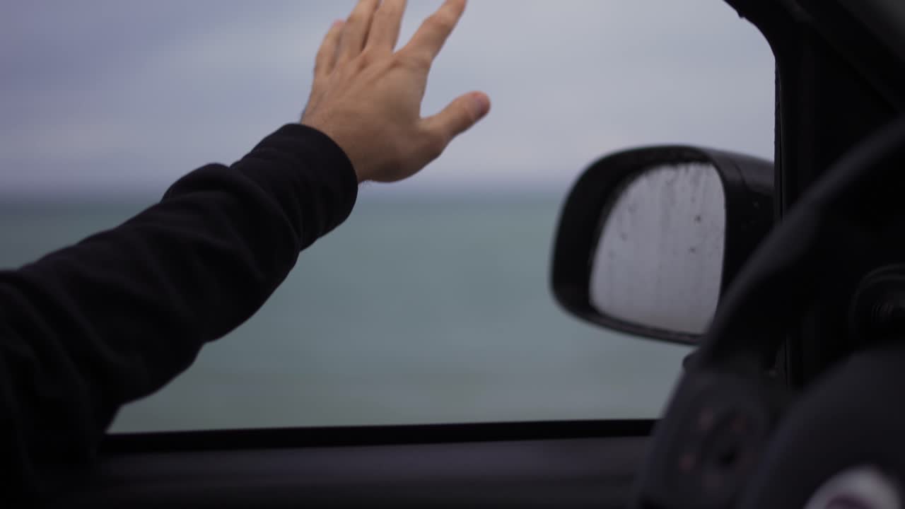 A man's hand is catching the rain out while driving a car on a rainy day
