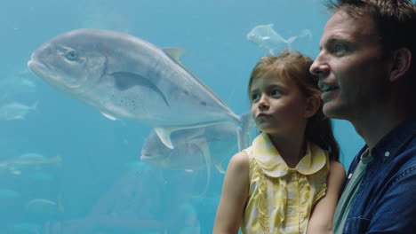 Glückliches-Mädchen-Mit-Vater-Im-Aquarium-Und-Blick-Auf-Fische,-Die-Im-Aquarium-Schwimmen.-Neugieriges-Kind,-Das-Neugierig-Das-Leben-Im-Meer-Beobachtet.-Vater-Bringt-Tochter-Im-Ozeanarium-Etwas-über-Meerestiere-Bei