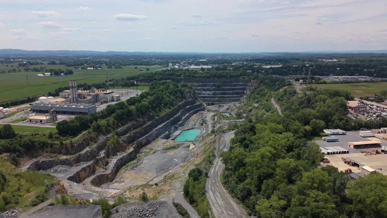 Cinematic drone footage flying over a turquoise quarry water basin surrounded by stone extraction pits and industrial terrain.