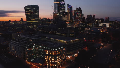 Evening-aerial-footage-of-group-of-modern-skyscrapers-in-City-business-hub-against-twilight-sky.-Working-overtime-in-office.-London,-UK