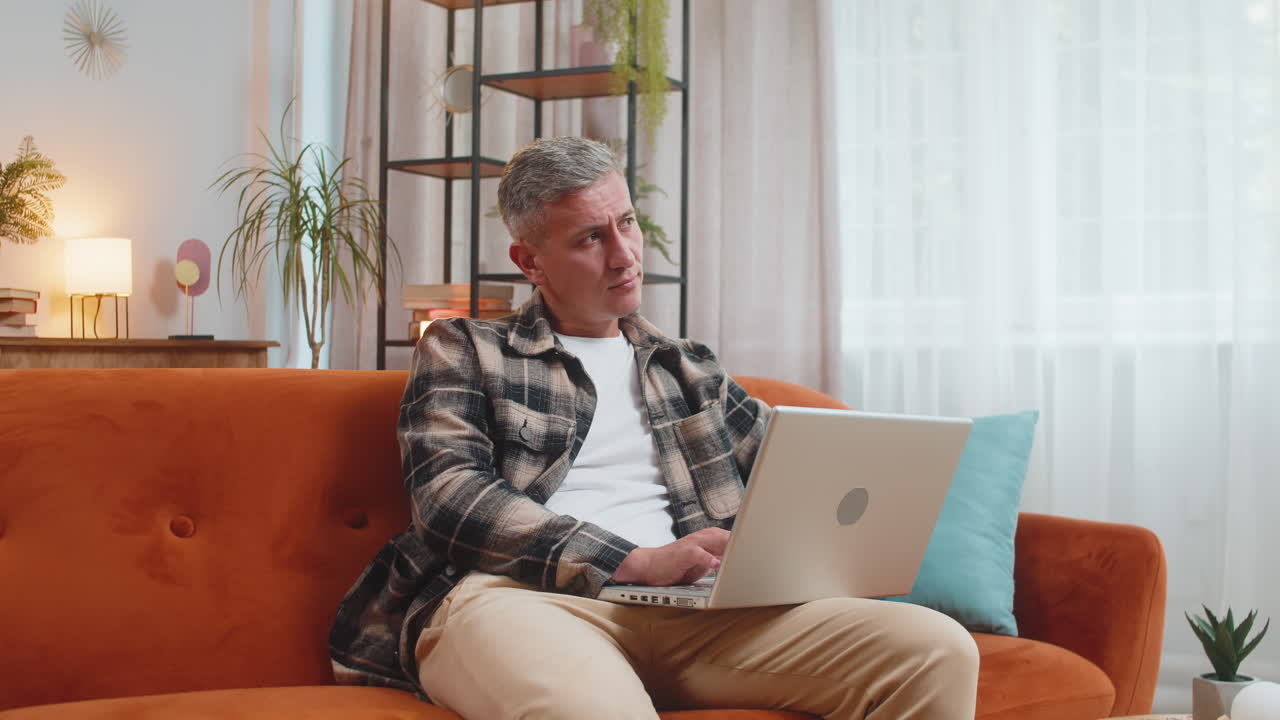 Man working on laptop computer with pensive expression pondering a solution answer at home room