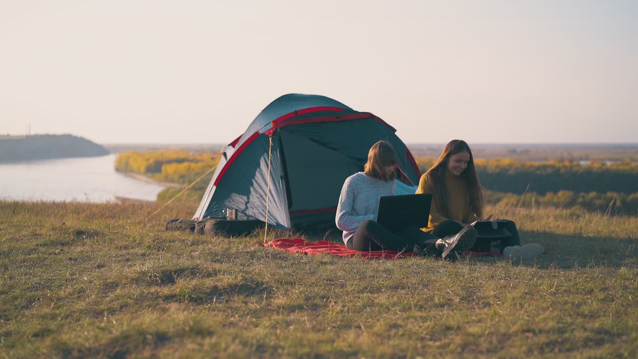 텐트 근처의 빨간 플레이드에 태블릿과 노트북을 가진 즐거운 소녀