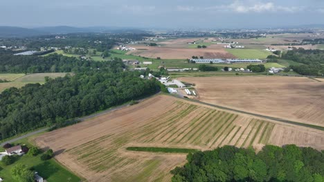 cloudy day in american countryside with farmsteads snd barns. aerial backwards wide shot. driving cars on suburb road. summer season in pennsylvania