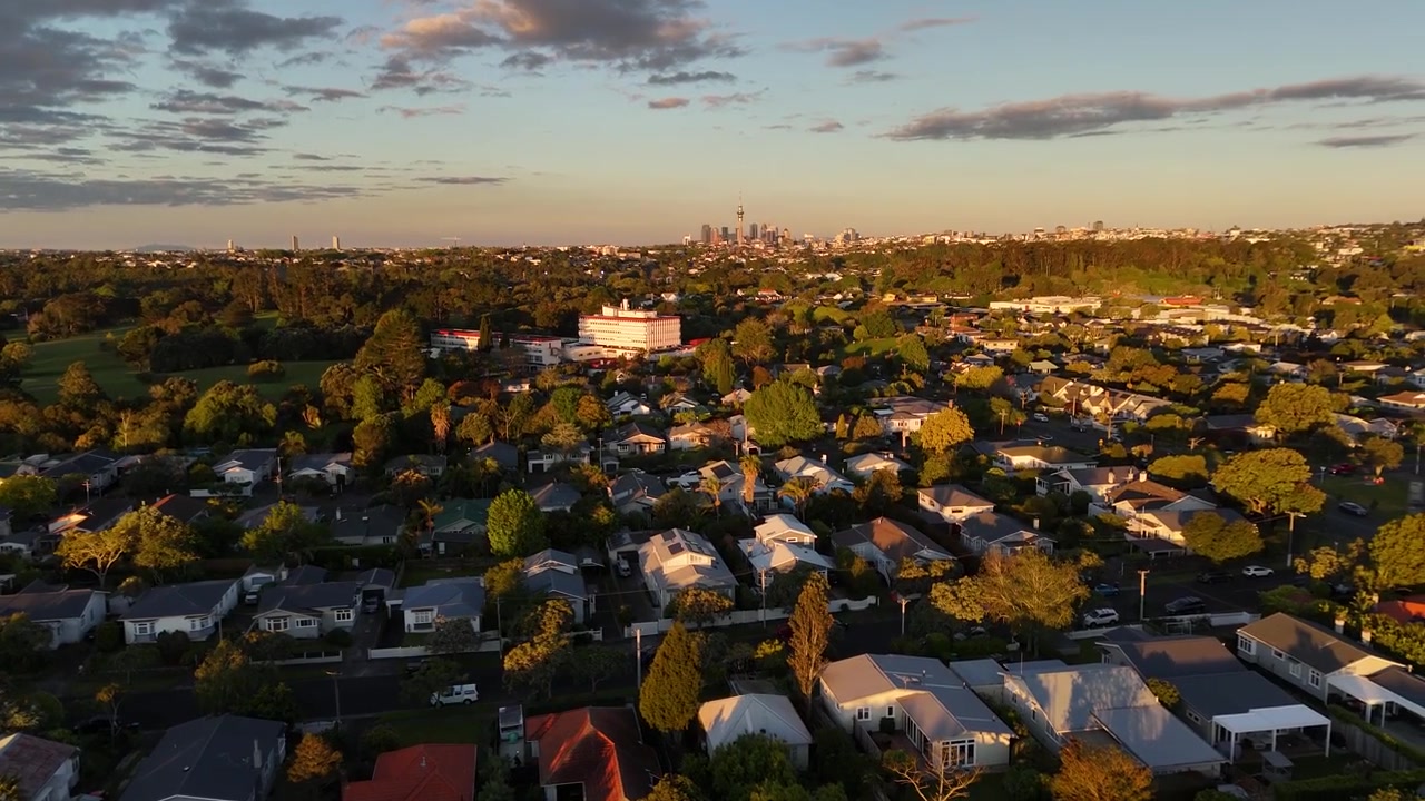 Vista aérea ascendente con dron 4K a 60 fps inclinándose sobre el tráfico de la ciudad al atardecer en los suburbios de Mount Albert en Auckland, Nueva Zelanda. Luz de la hora dorada iluminando las calles residenciales.