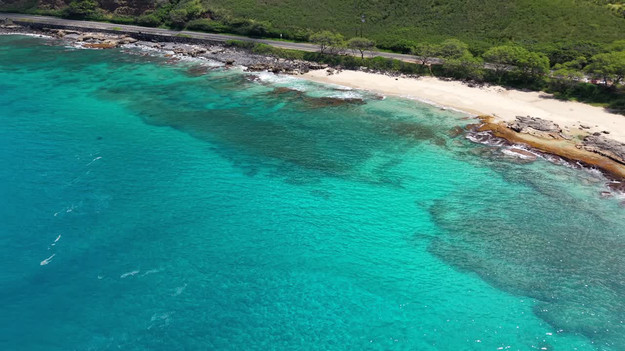 Secluded sandy cove and turquoise water next to a coastal highway in Oahu, Hawaii